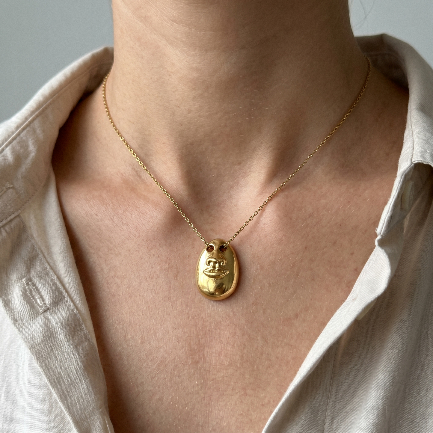 See No Evil Pendant Necklace in gold worn on a delicate chain with a relaxed beige shirt.