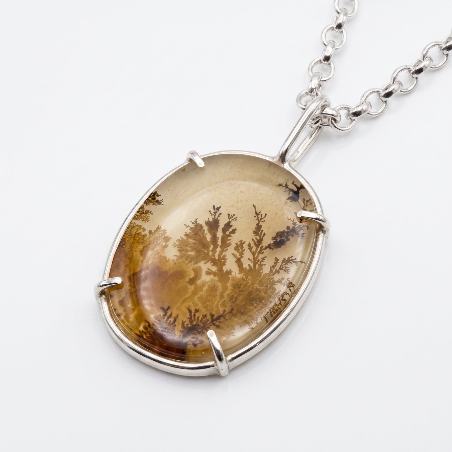 An oval pendant necklace featuring a translucent amber-brown stone with a detailed botanical or coral-like pattern, set in a polished silver-tone bezel and chain.