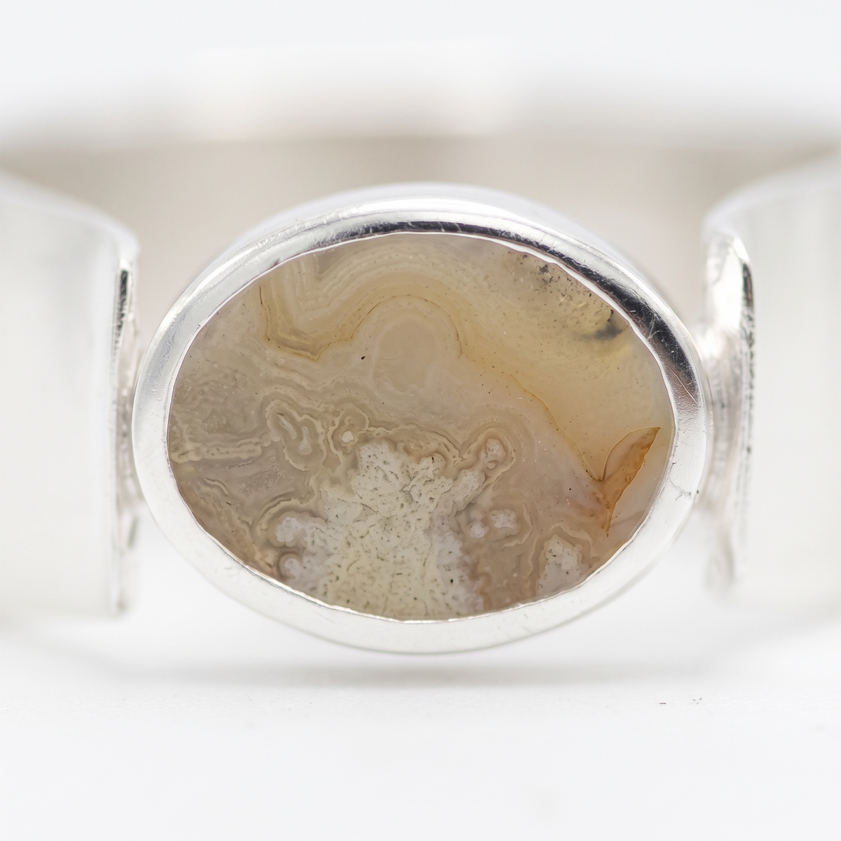 A silver ring featuring an oval cabochon stone with natural agate or jasper banded patterns in beige, cream, and light brown tones.
