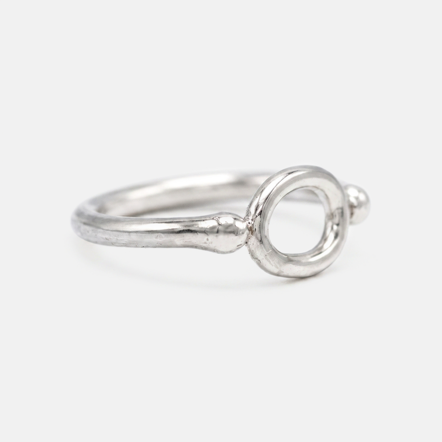 A silver ring with a textured band and a circular openwork top, photographed on a light gray background.