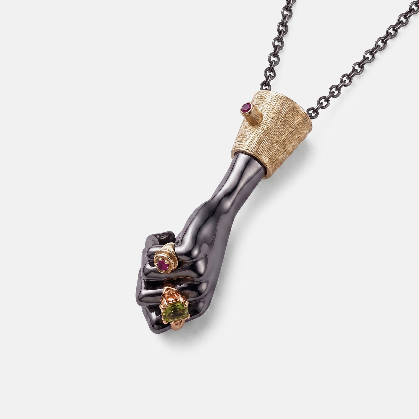 Close-up black hand pendant in gold setting with ruby and peridot stones, artistic fine jewellery necklace