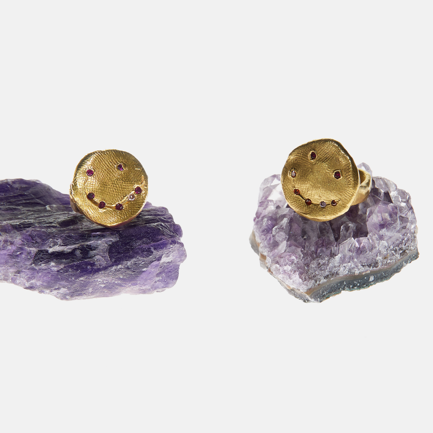 Gold earrings with embedded gemstones on purple crystal bases against a white background