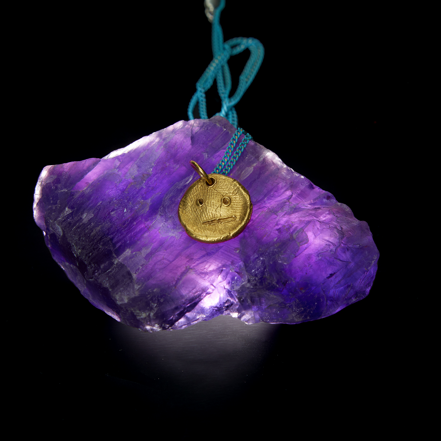 Gold sculptural pendant necklace styled with purple crystal