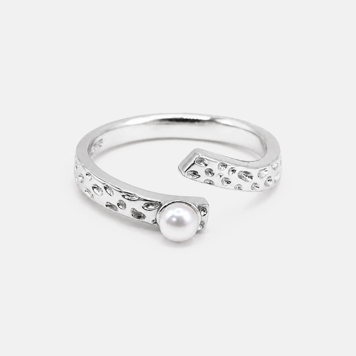 A silver open cuff ring featuring a textured, dotted border and a single white pearl set in the center, photographed on a light gray background.