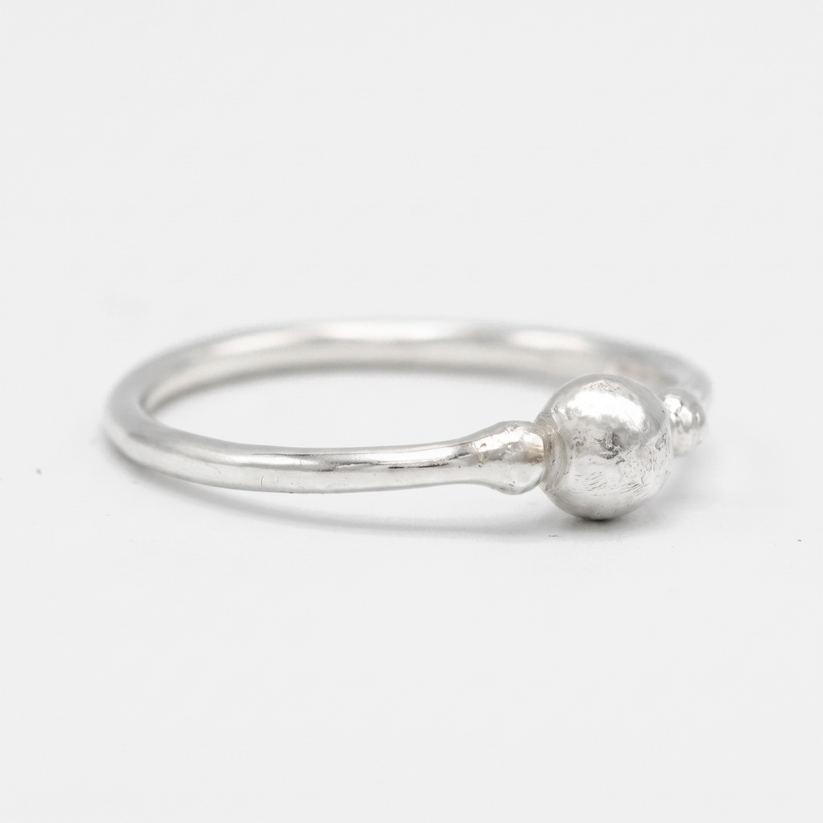 A silver ring with a textured, hammered finish and a small spherical bead detail on the band, photographed on a clean white background.