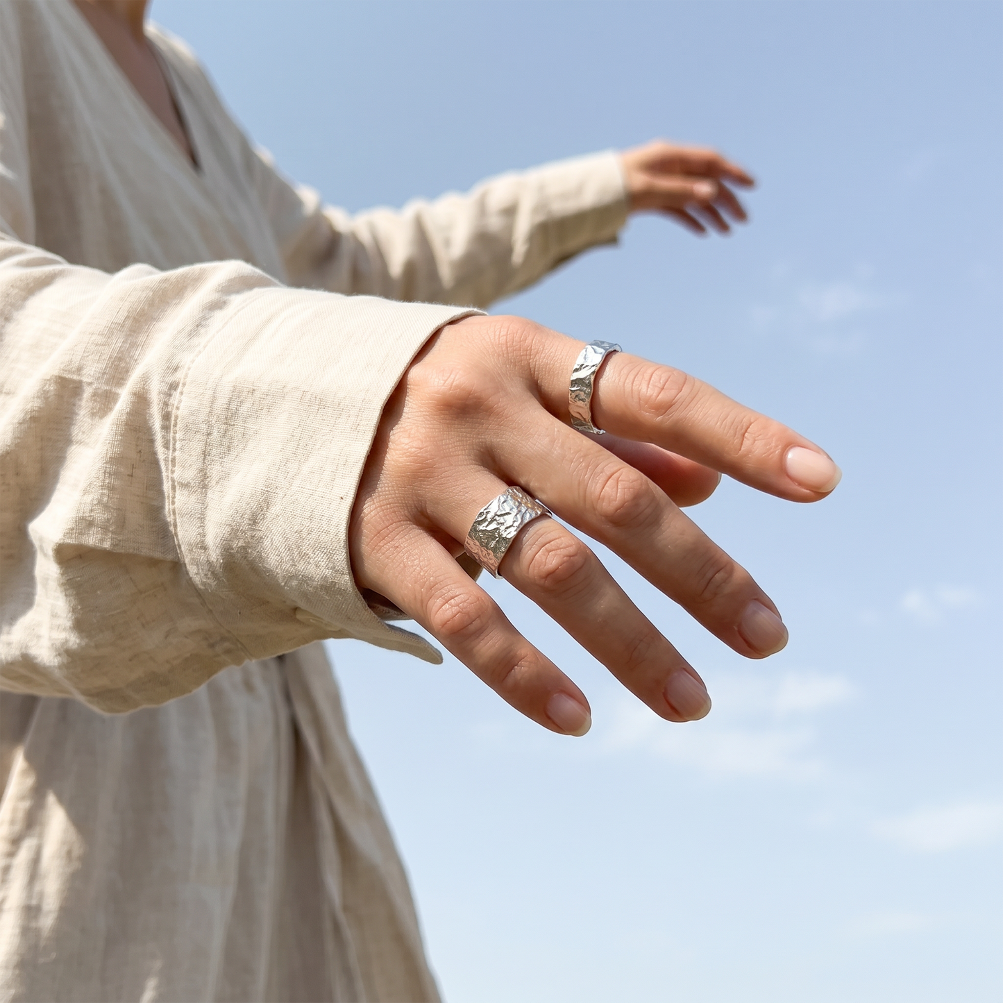 Person wearing two silver rings on a blurred blue sky background