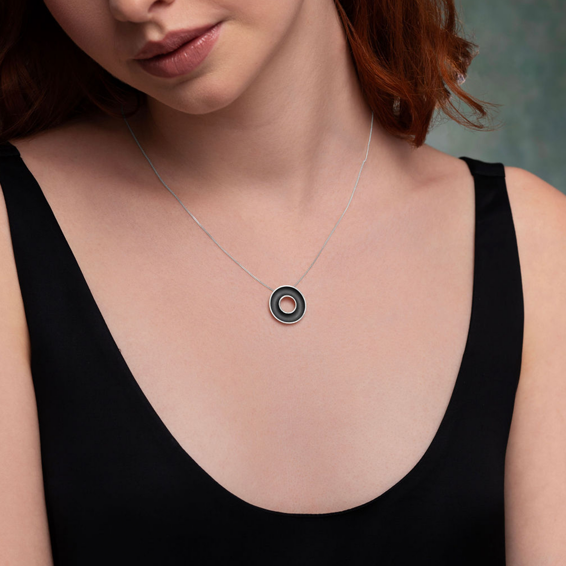 Woman wearing a necklace with a circular pendant against a neutral background