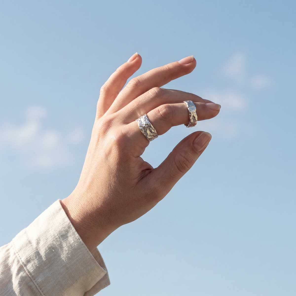 Hand wearing two rings with a clear blue sky background