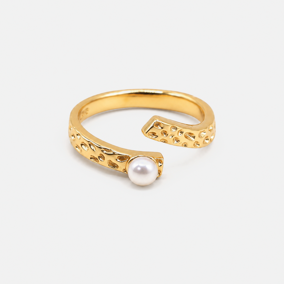 A gold open-bend ring featuring textured, hammered details and a single white pearl set in one of the ends, photographed on a clean, light gray background.