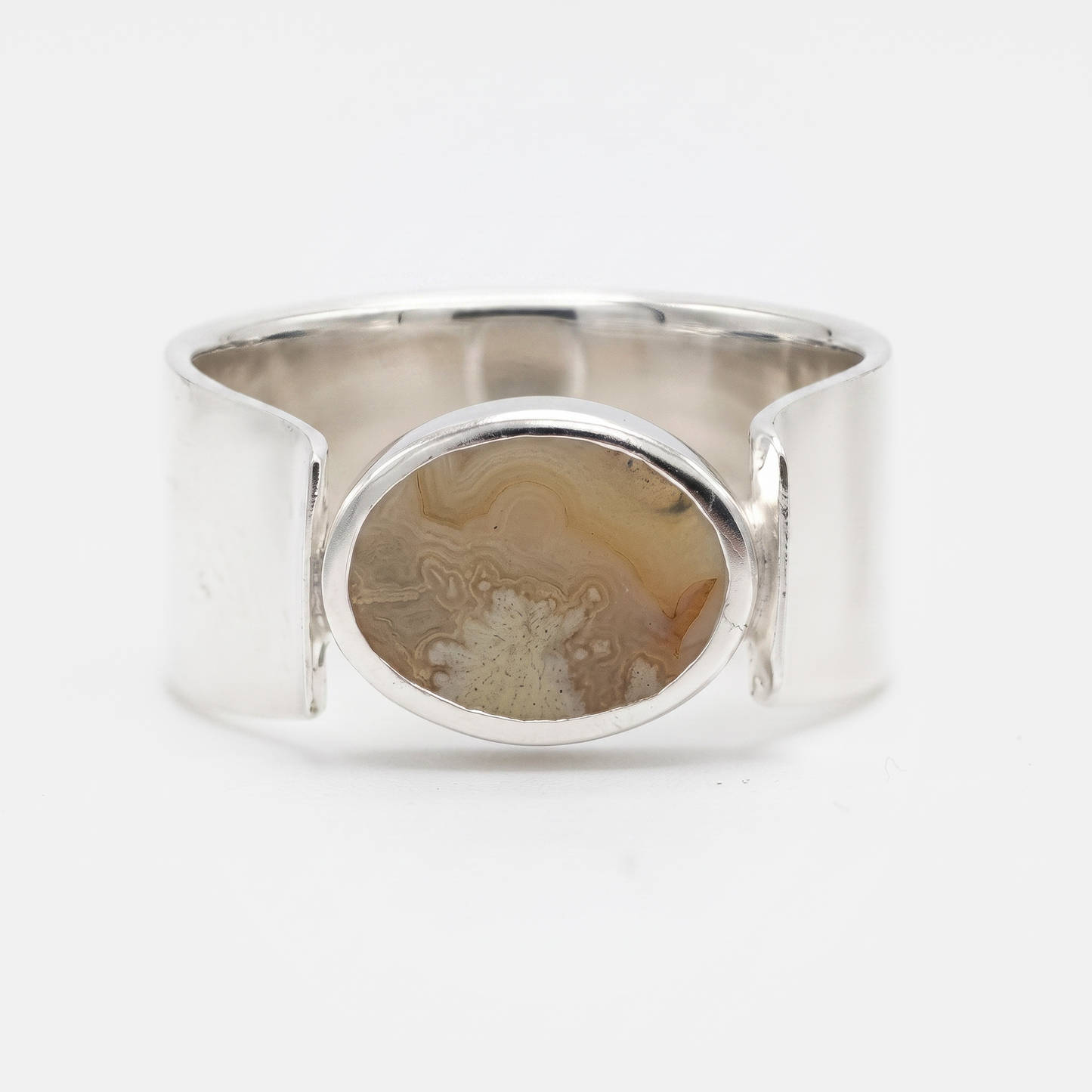 A wide silver cuff ring featuring a central oval bezel set with a natural agate stone showing brown and beige banded patterns, photographed on a clean white background.