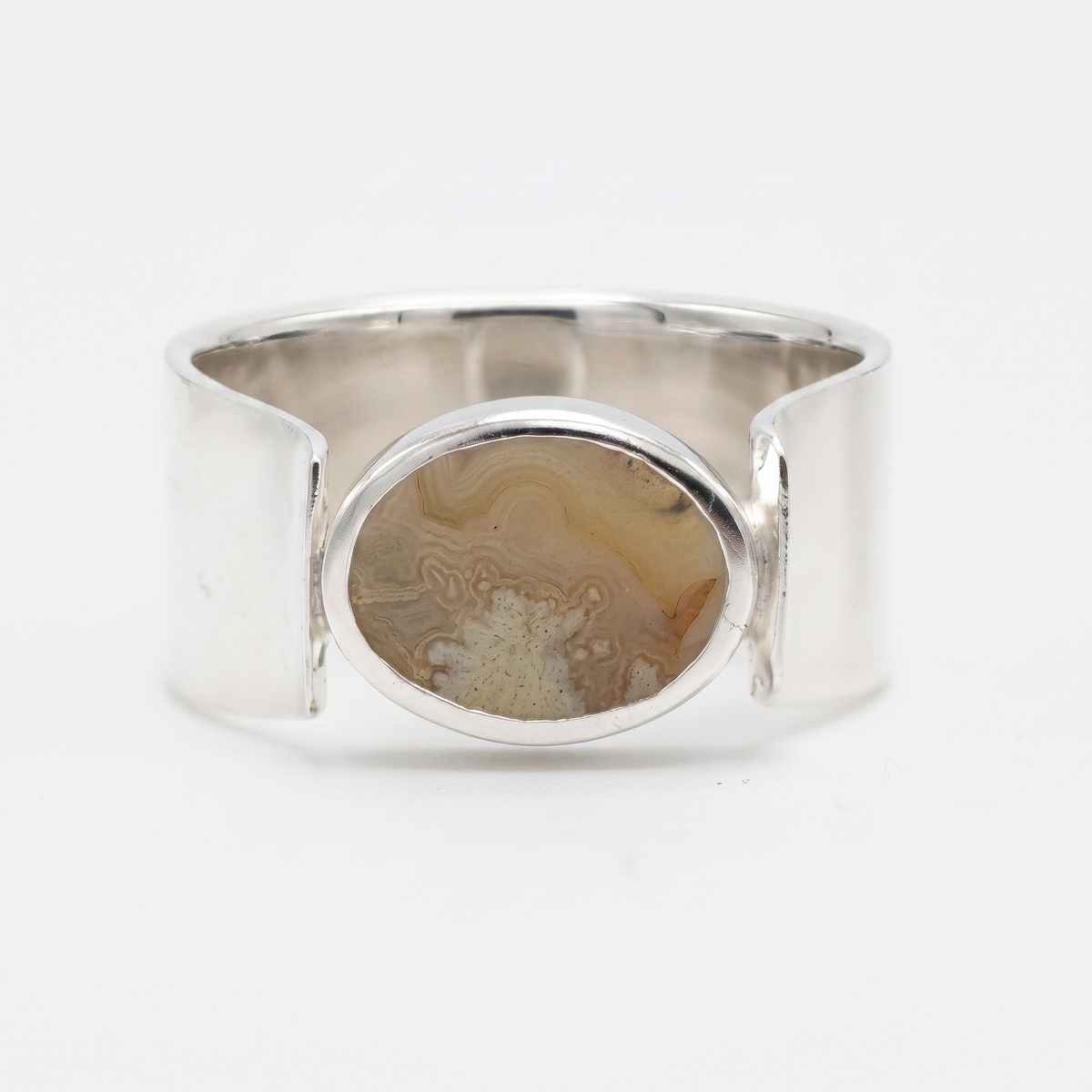 A wide silver cuff ring featuring a central oval bezel set with a natural agate stone showing brown and beige banded patterns, photographed on a clean white background.