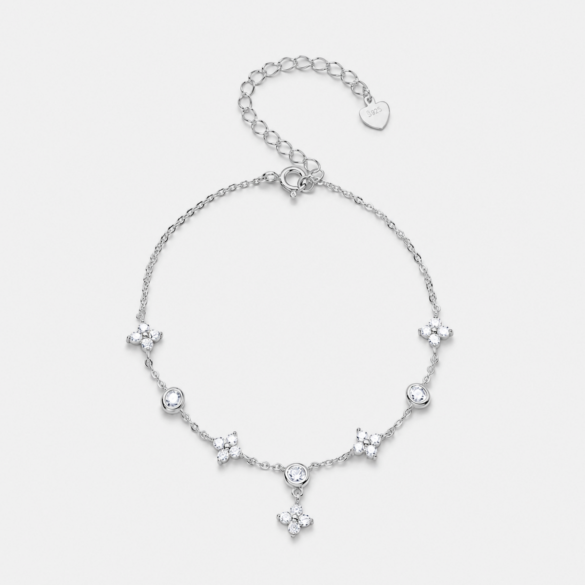 A delicate silver chain bracelet featuring five small floral star motifs and a central round clear stone, with an adjustable lobster clasp and heart-shaped tag, shown on a light gray background.