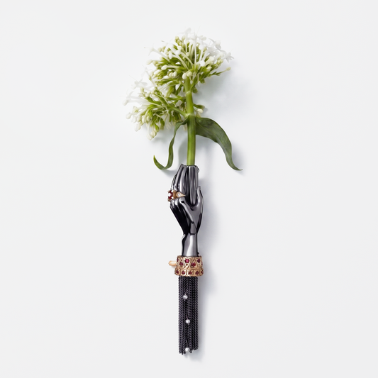 Black hand brooch holding white flower with gold and ruby details, luxury designer statement jewellery