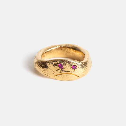 Gold ring with two red gemstones on a light gray background