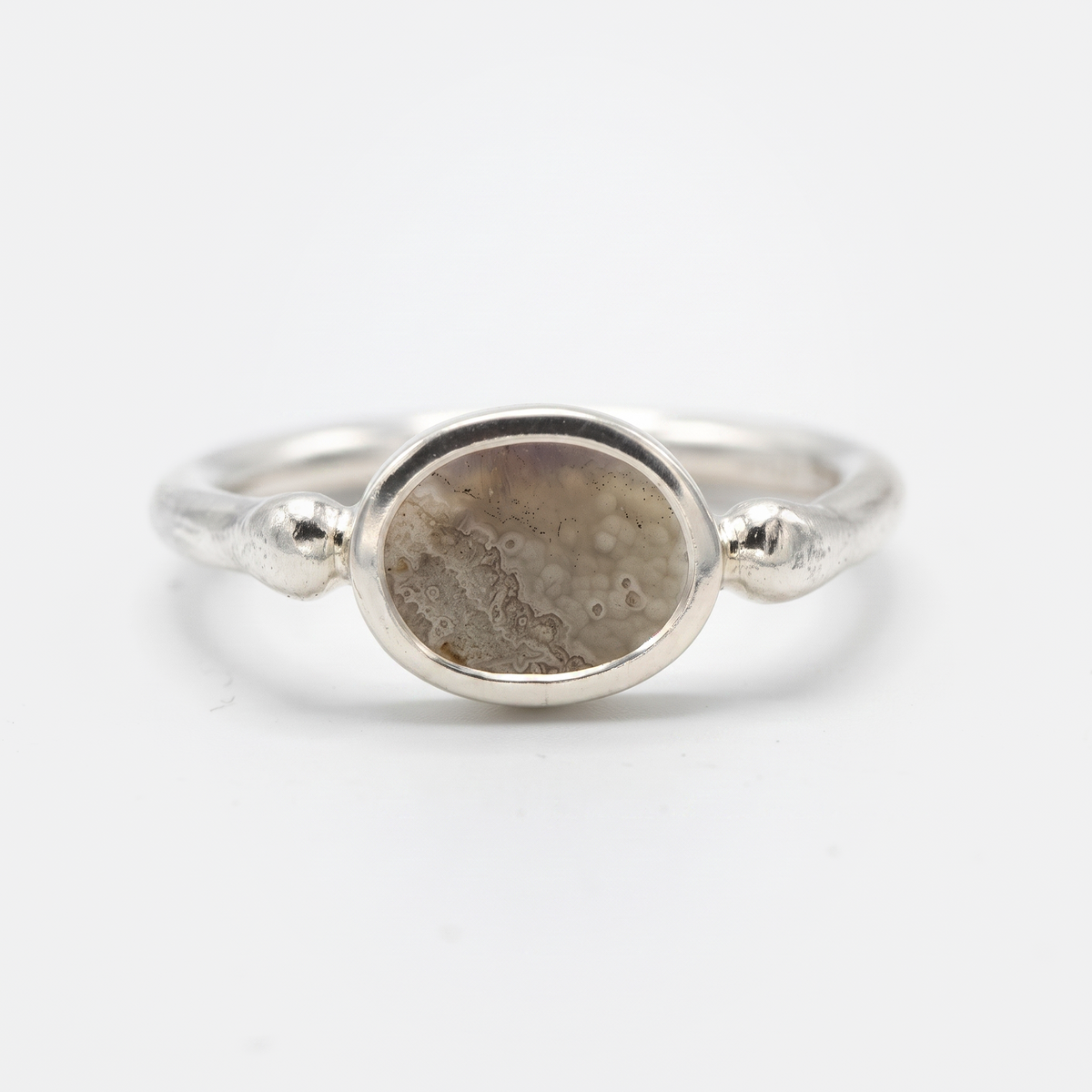 A silver ring featuring an oval-shaped stone with a textured, dappled pattern in shades of brown and gray, set against a clean white background.