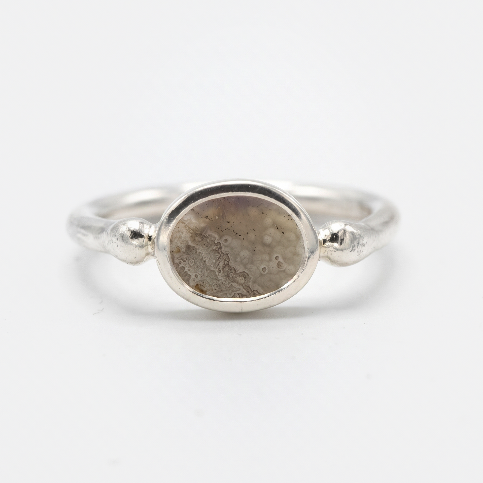 A silver ring featuring an oval-shaped stone with a textured, dappled pattern in shades of brown and gray, set against a clean white background.