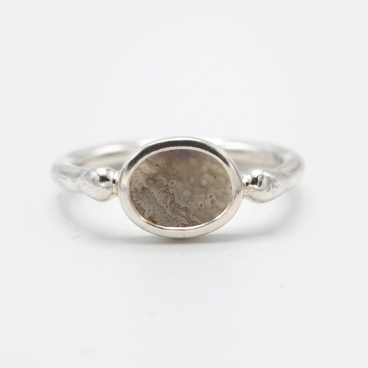 A silver ring featuring an oval-shaped stone with a textured, dappled pattern in shades of brown and gray, set against a clean white background.