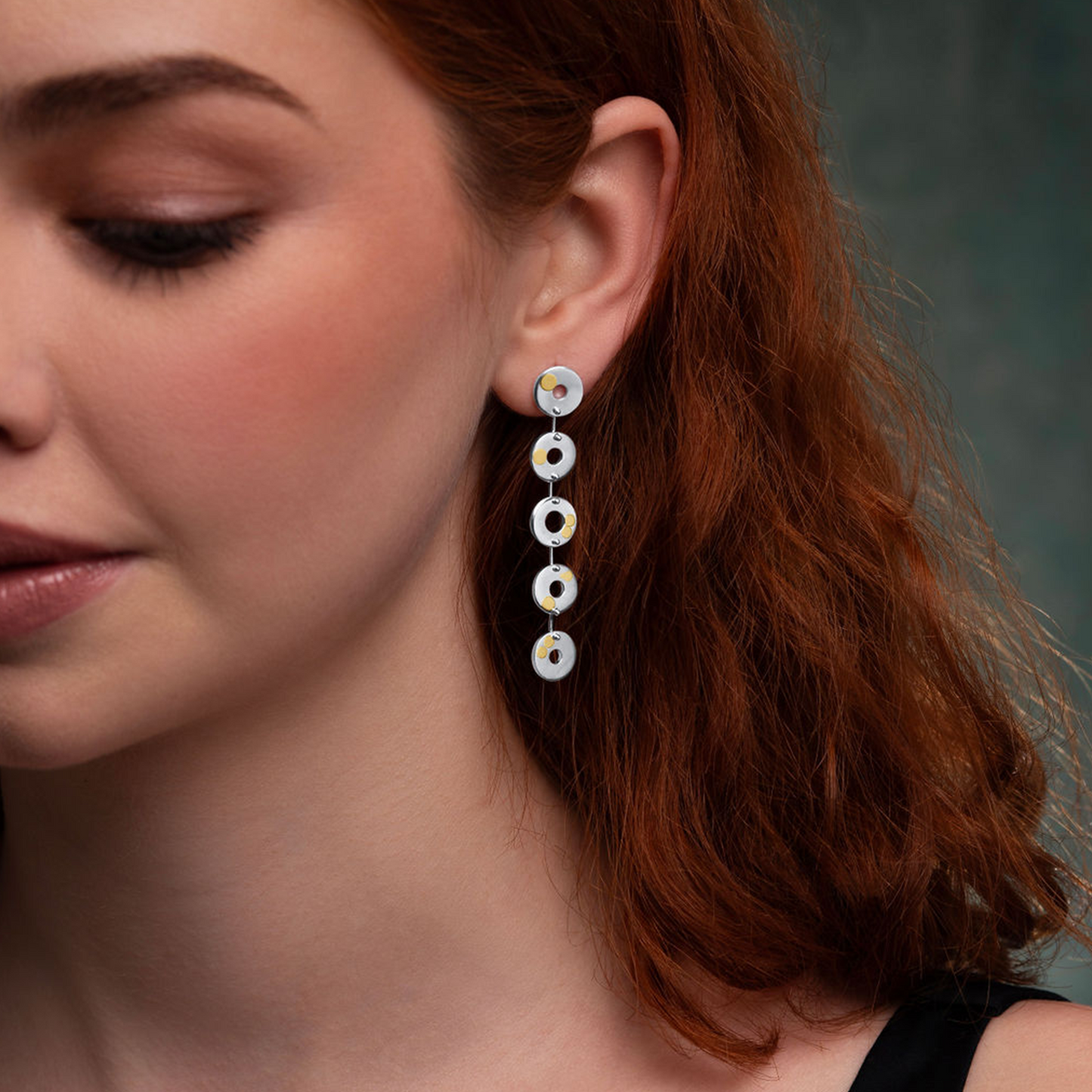 Close-up of a woman wearing a pair of dangling earrings with a neutral background