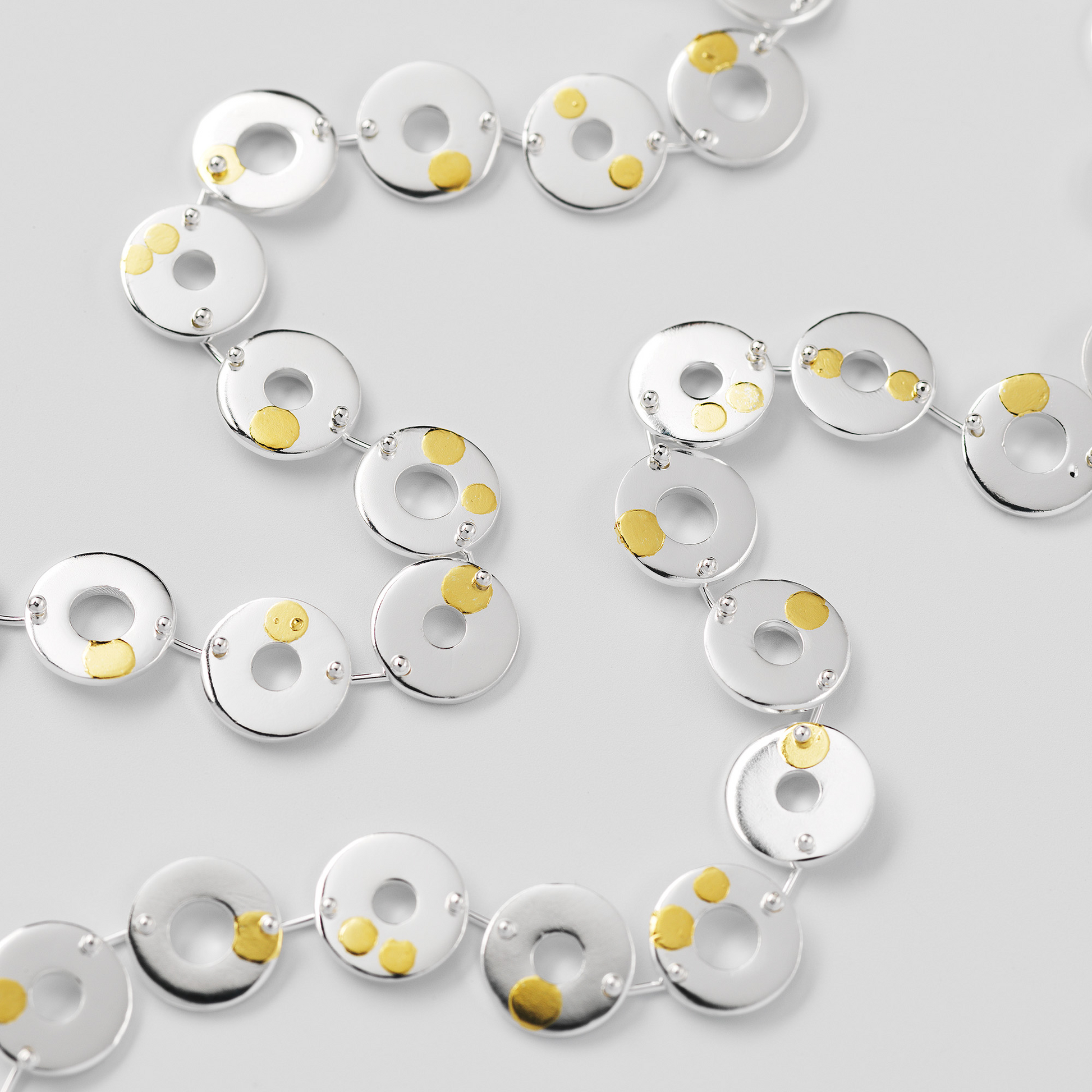 Silver necklace with circular links and gold accents on a light gray background