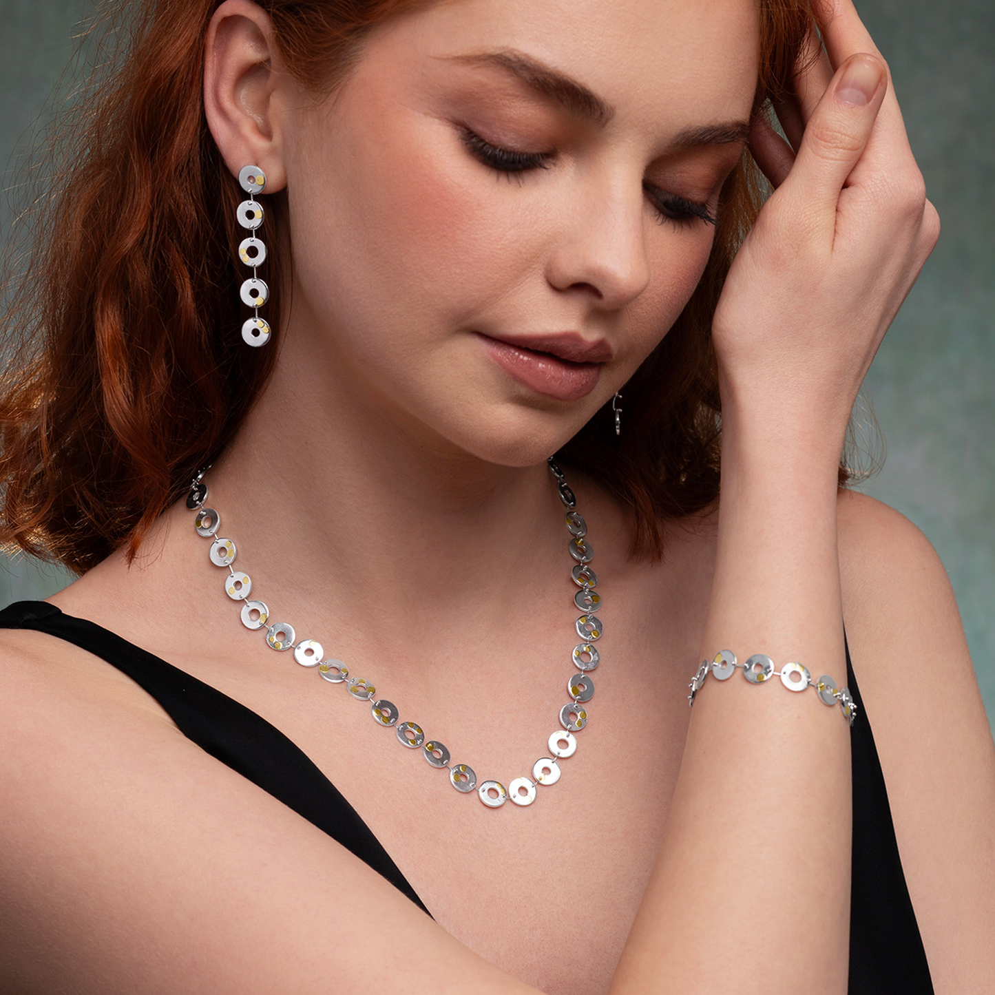 Woman wearing silver jewelry including earrings, necklace, and bracelet against a neutral background