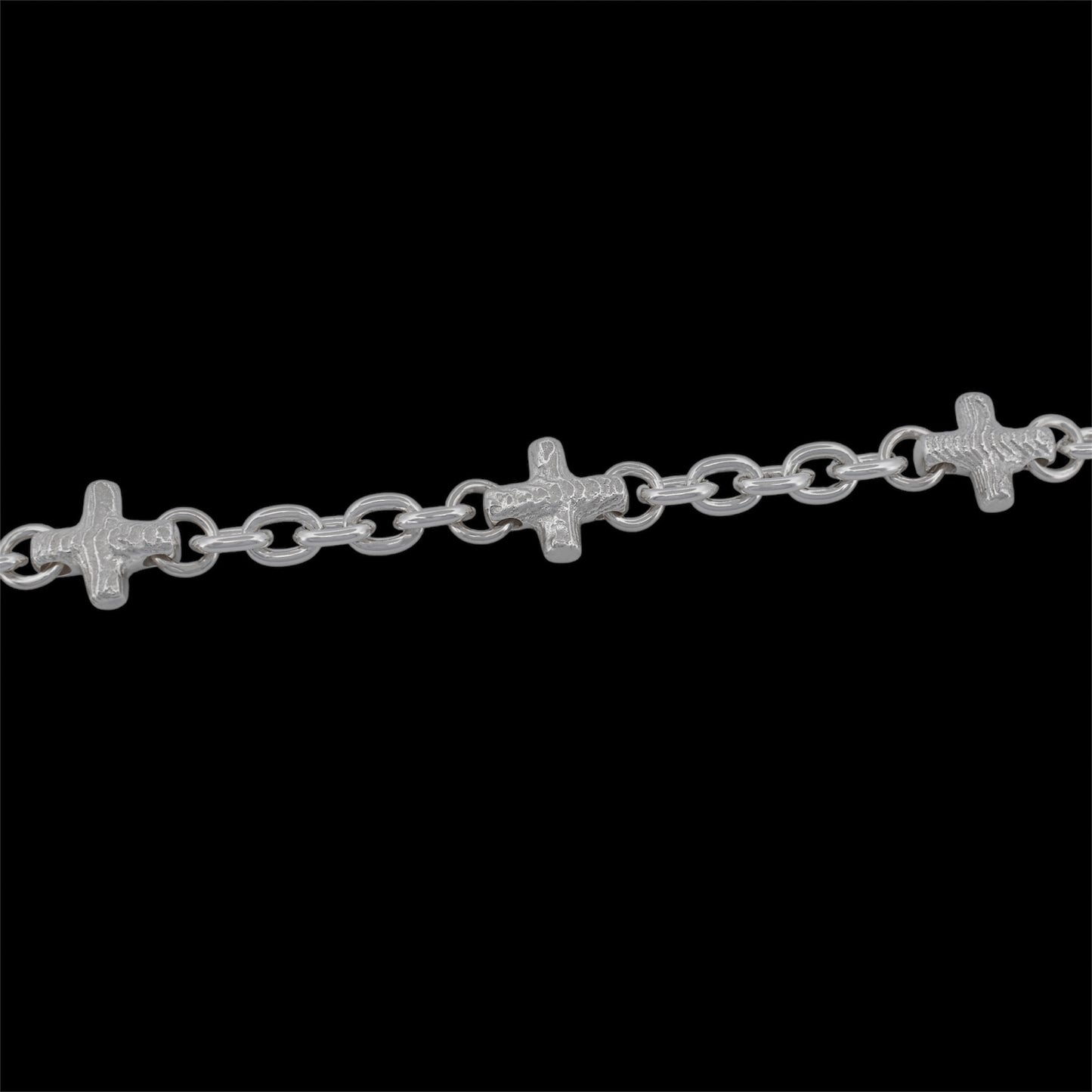 A silver chain bracelet featuring three small, detailed crucifix links spaced evenly along a dark black background.