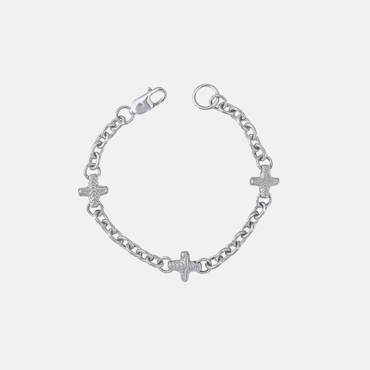 A silver chain bracelet featuring three small cross charms, one of which is adorned with a textured pavé diamond, shown on a light gray background.