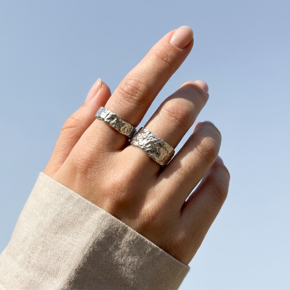 Hand wearing two silver rings with a clear blue sky background