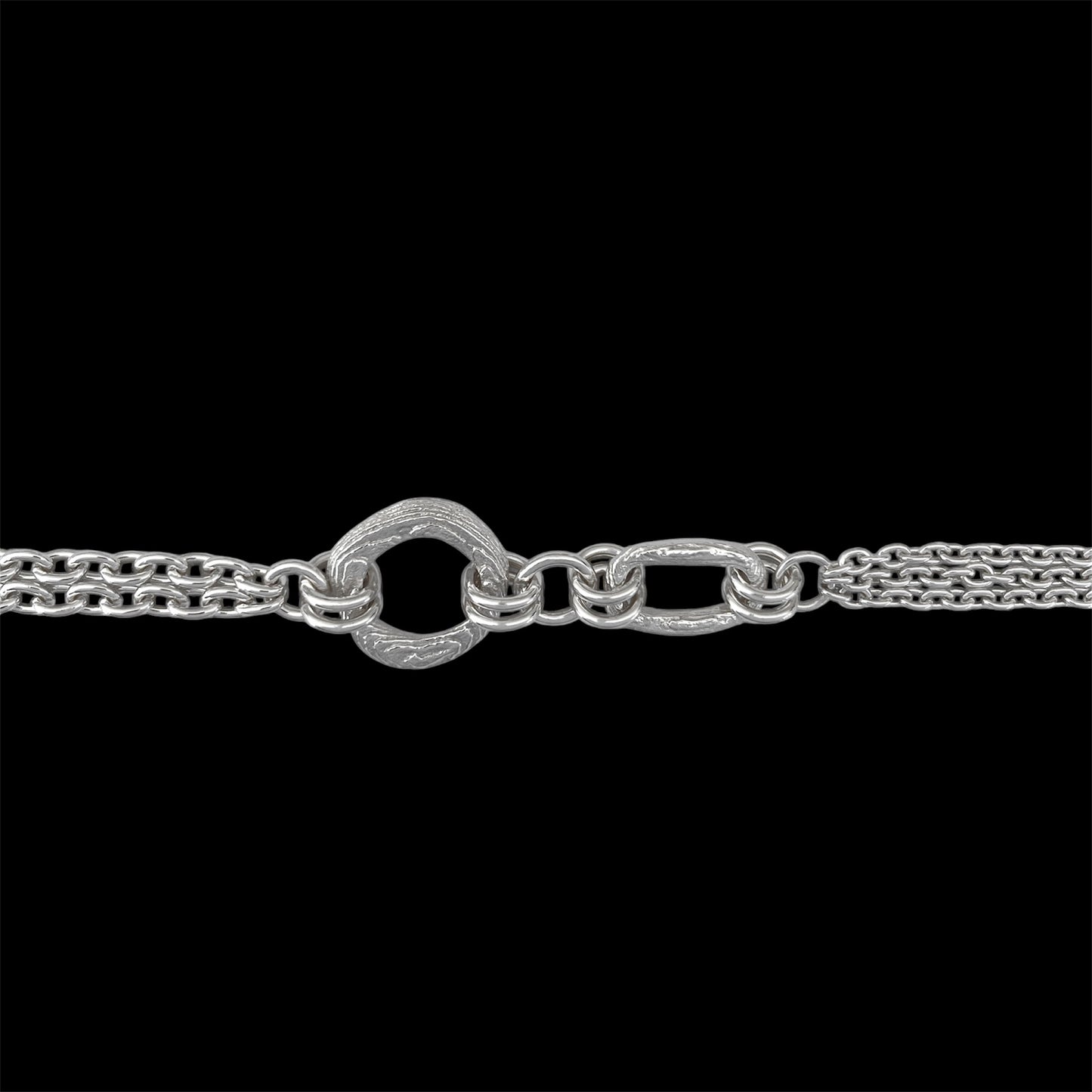 A close-up of a silver-toned chain necklace featuring a distinctive textured heart-shaped clasp connected to elongated oval links, set against a solid black background.