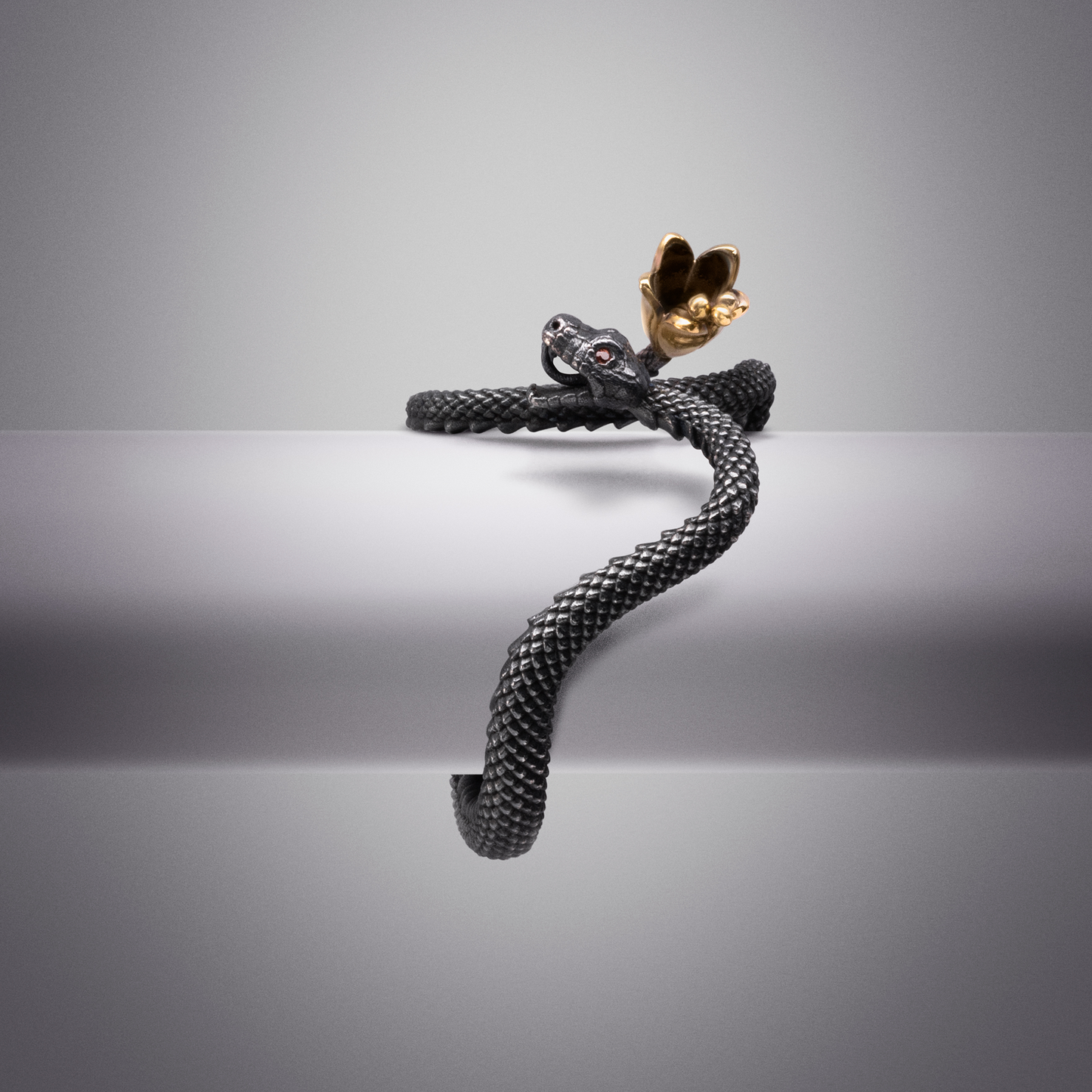 Statement snake ring with textured black scales and gold hand motif, modern sculptural jewellery
