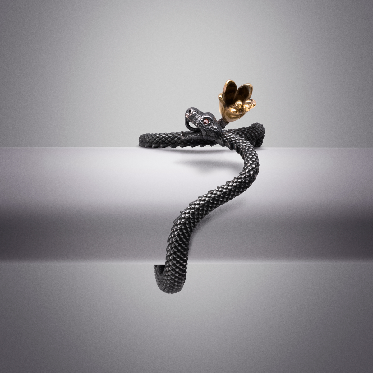 Statement snake ring with textured black scales and gold hand motif, modern sculptural jewellery
