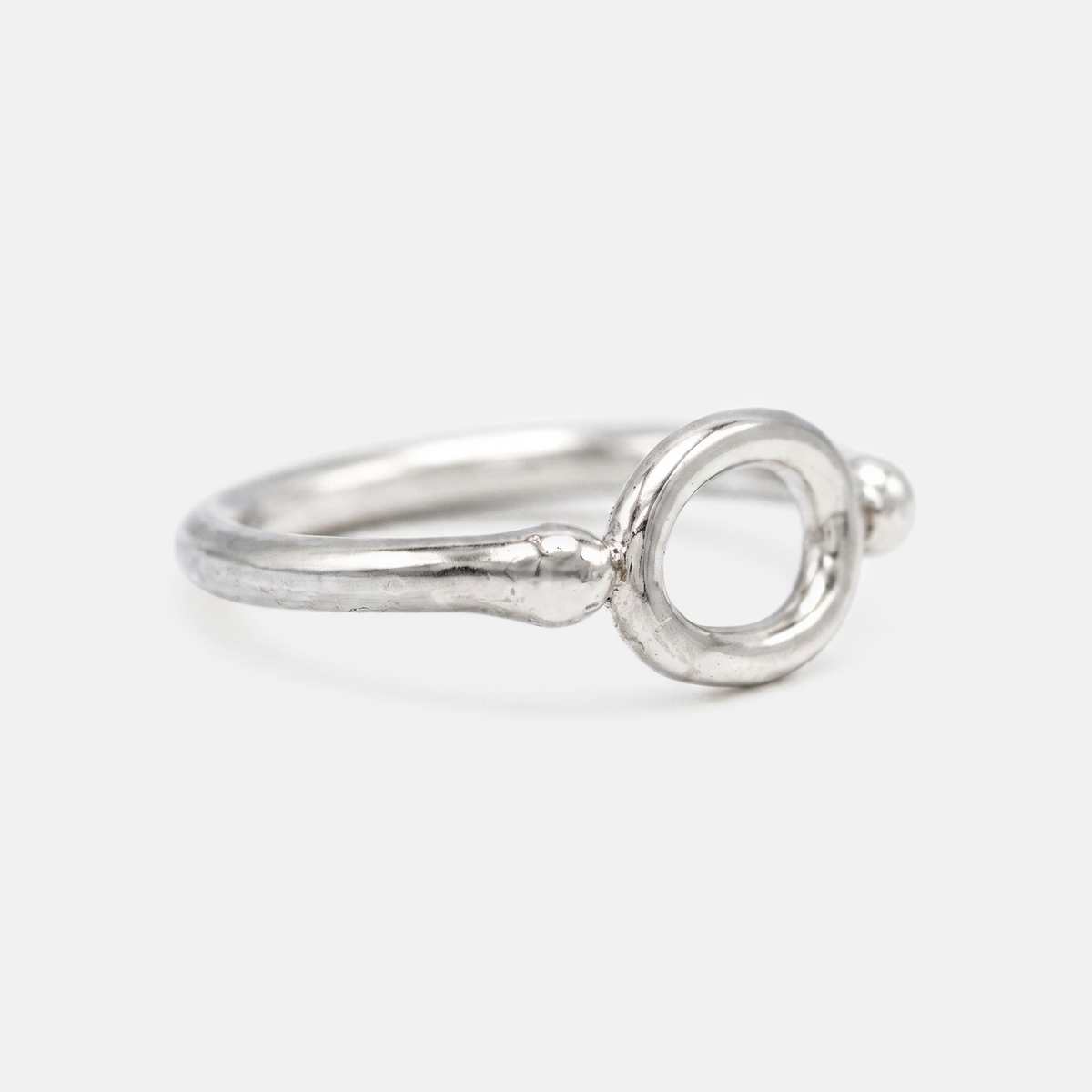 A silver ring with a textured band and a circular openwork top, photographed on a light gray background.