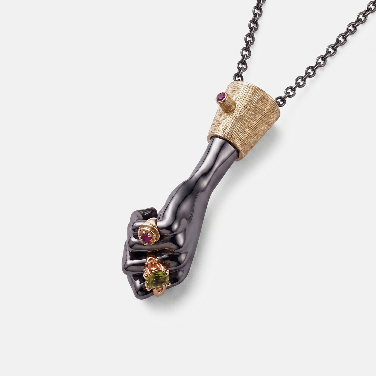 Close-up black hand pendant in gold setting with ruby and peridot stones, artistic fine jewellery necklace