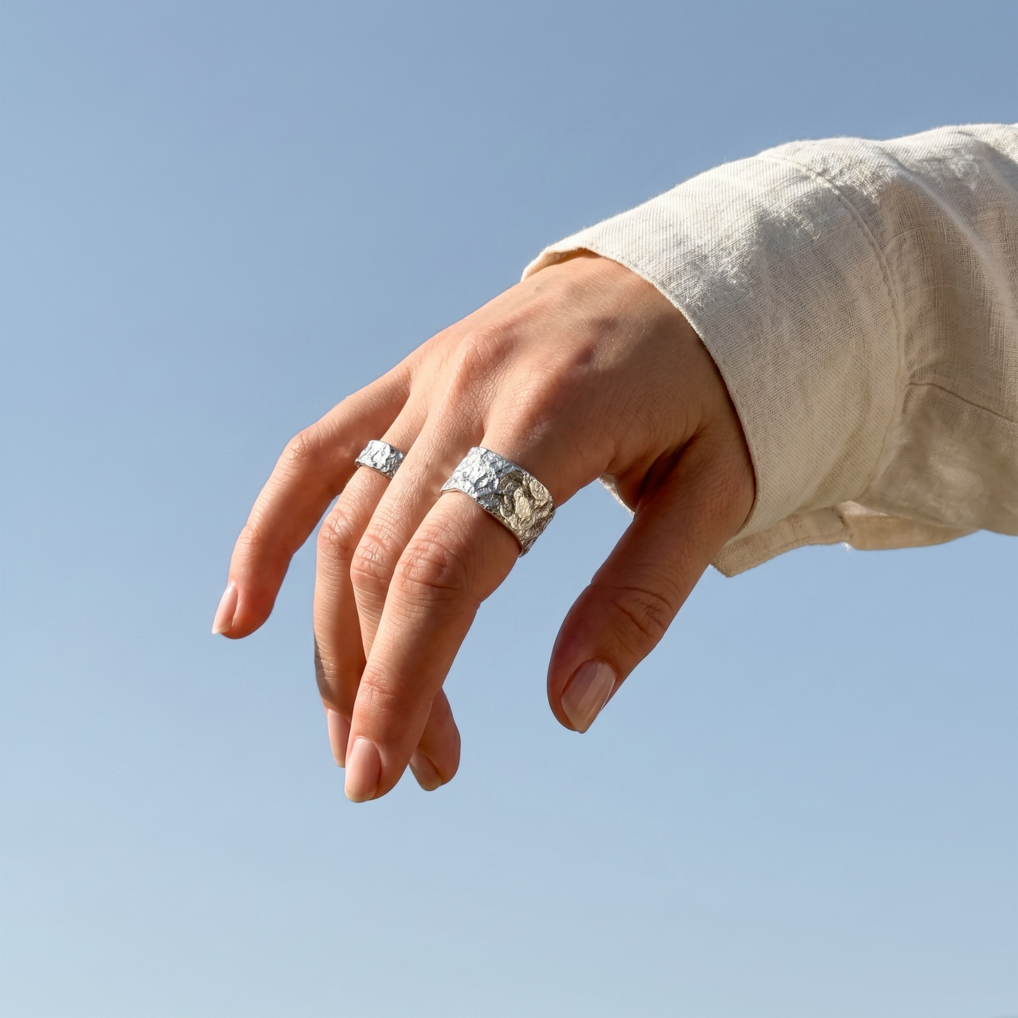 Hand wearing two silver rings against a clear blue sky
