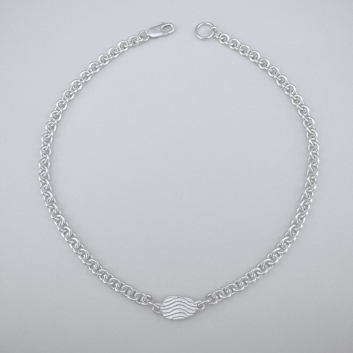 Silver chain bracelet with a wave design on a light gray background