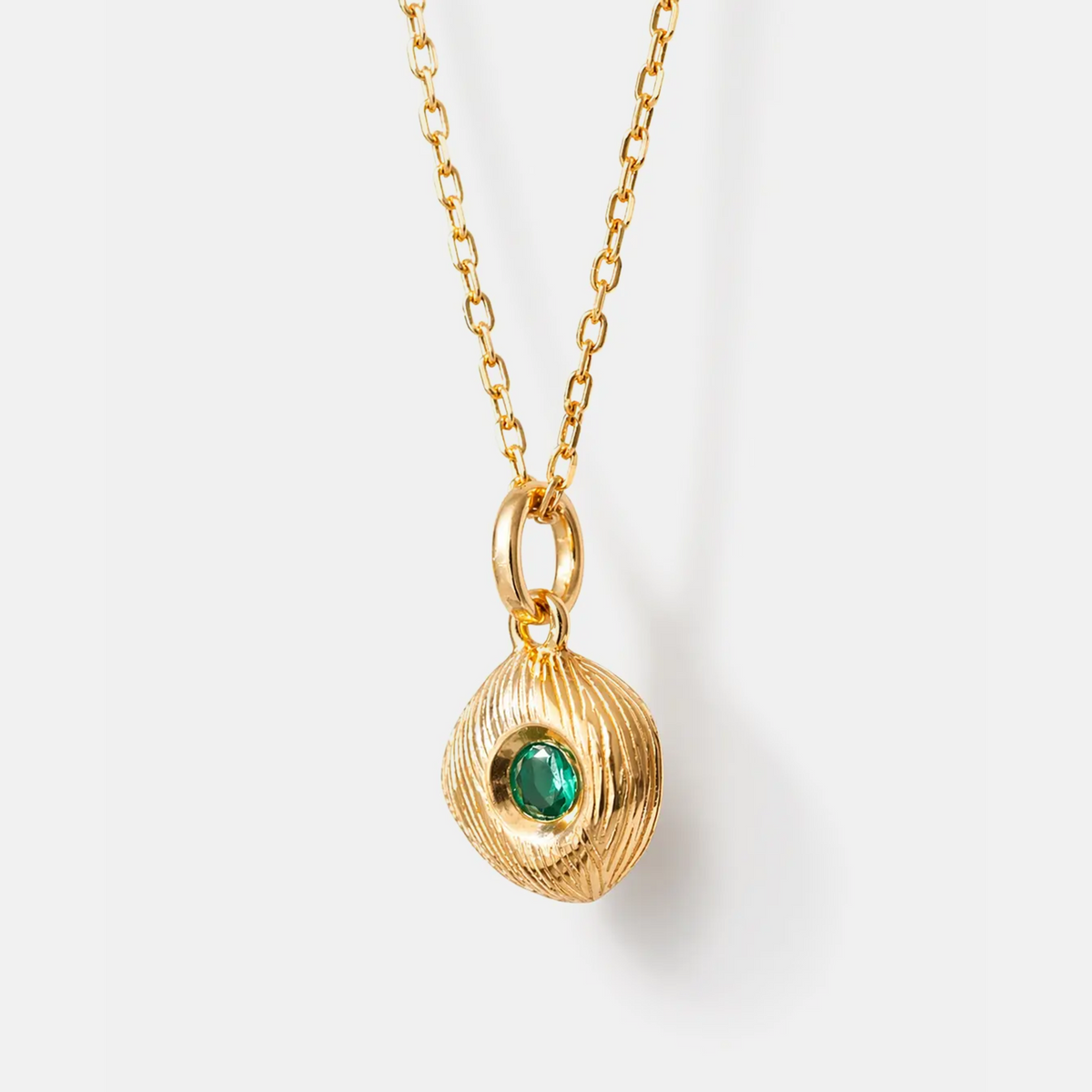 A gold chain necklace with a textured, organic-shaped gold pendant featuring a small, round green gemstone in the center, shown against a clean white background.