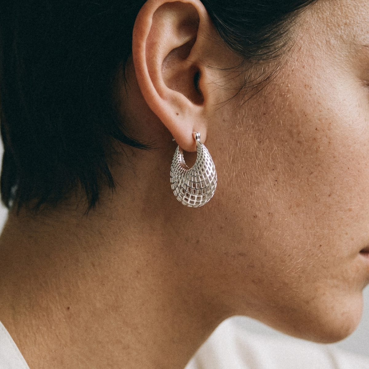 A close-up side profile of a woman wearing a textured silver crescent hoop earring.