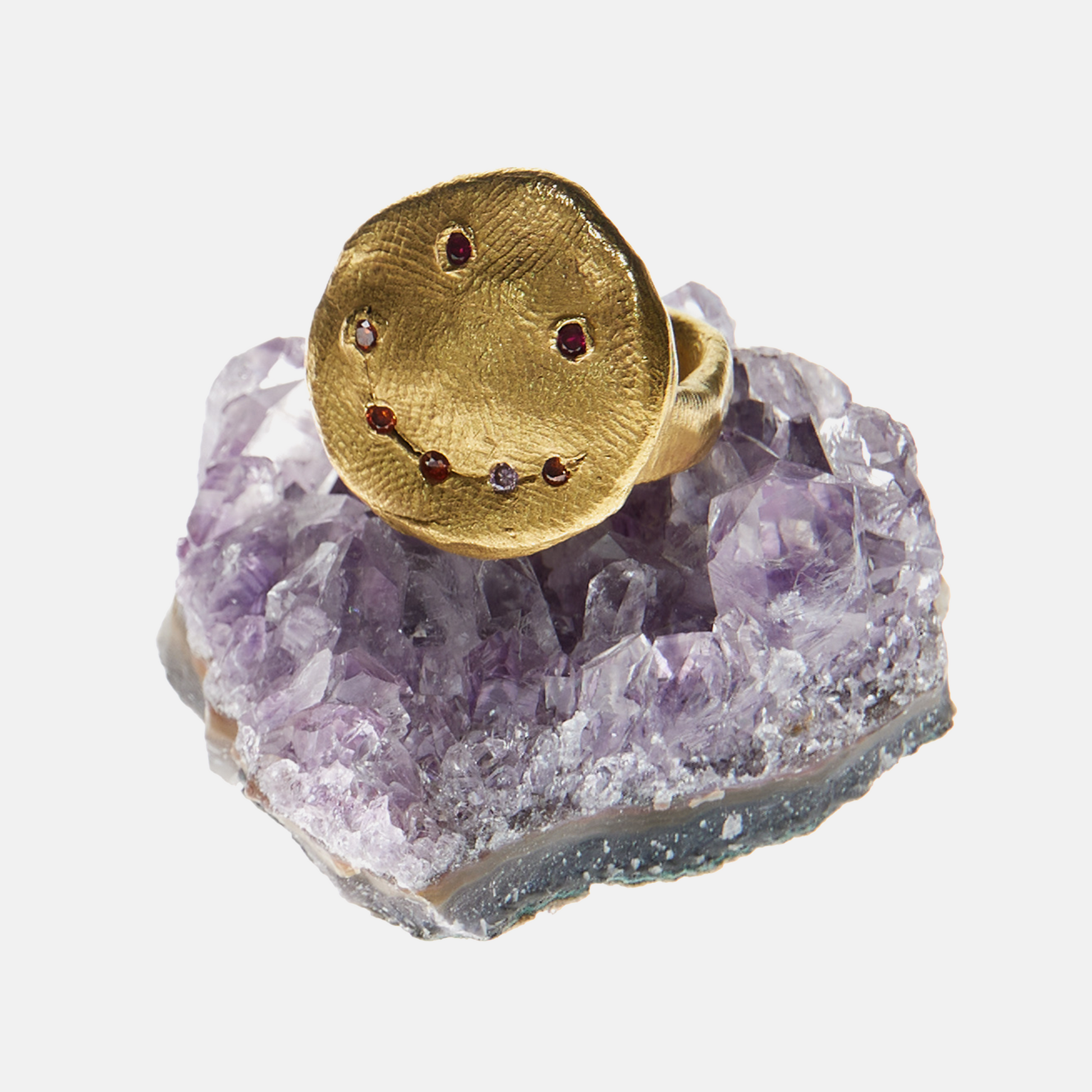 Gold ring with embedded red stones on a purple crystal base