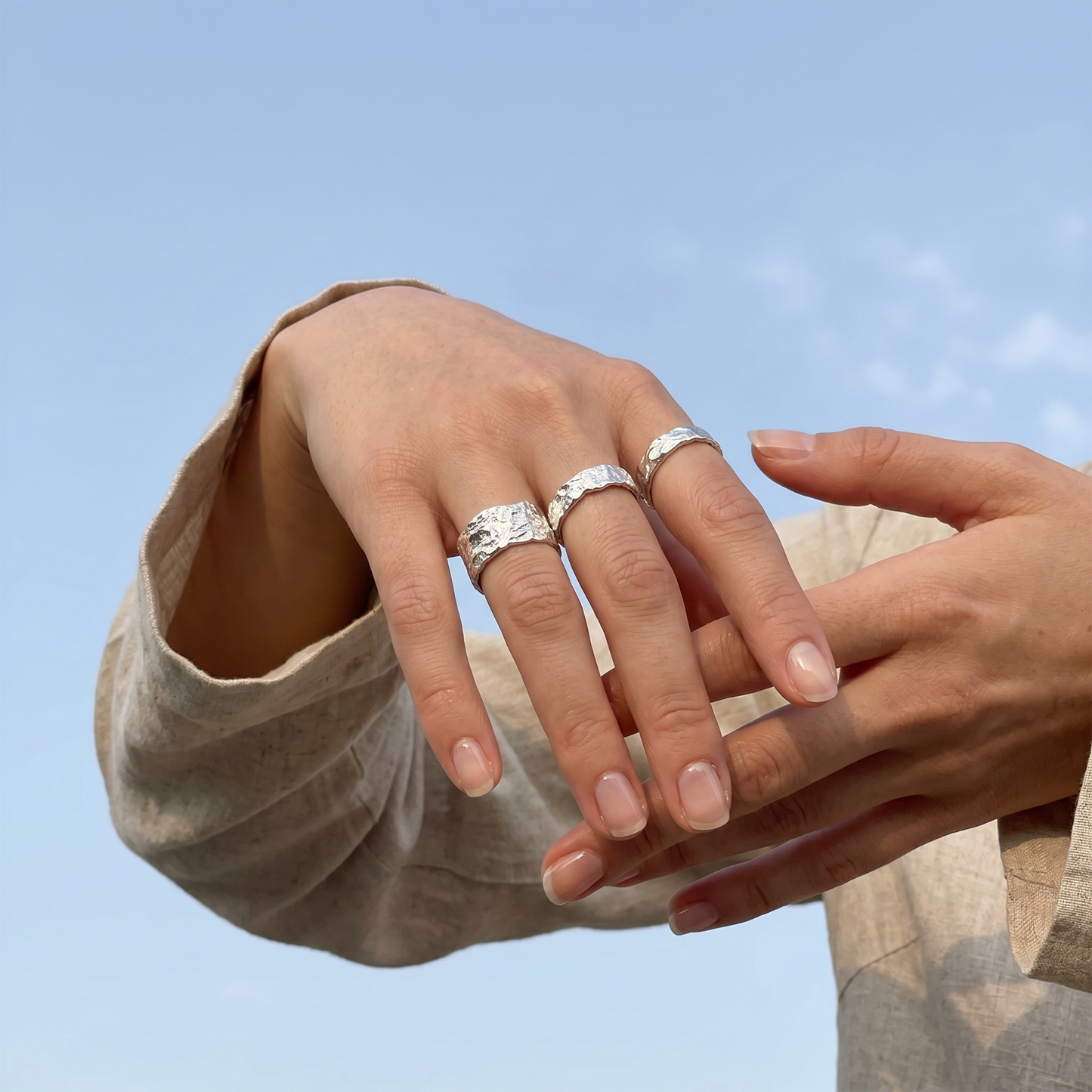 Close-up of hands wearing silver rings against a light blue sky.
