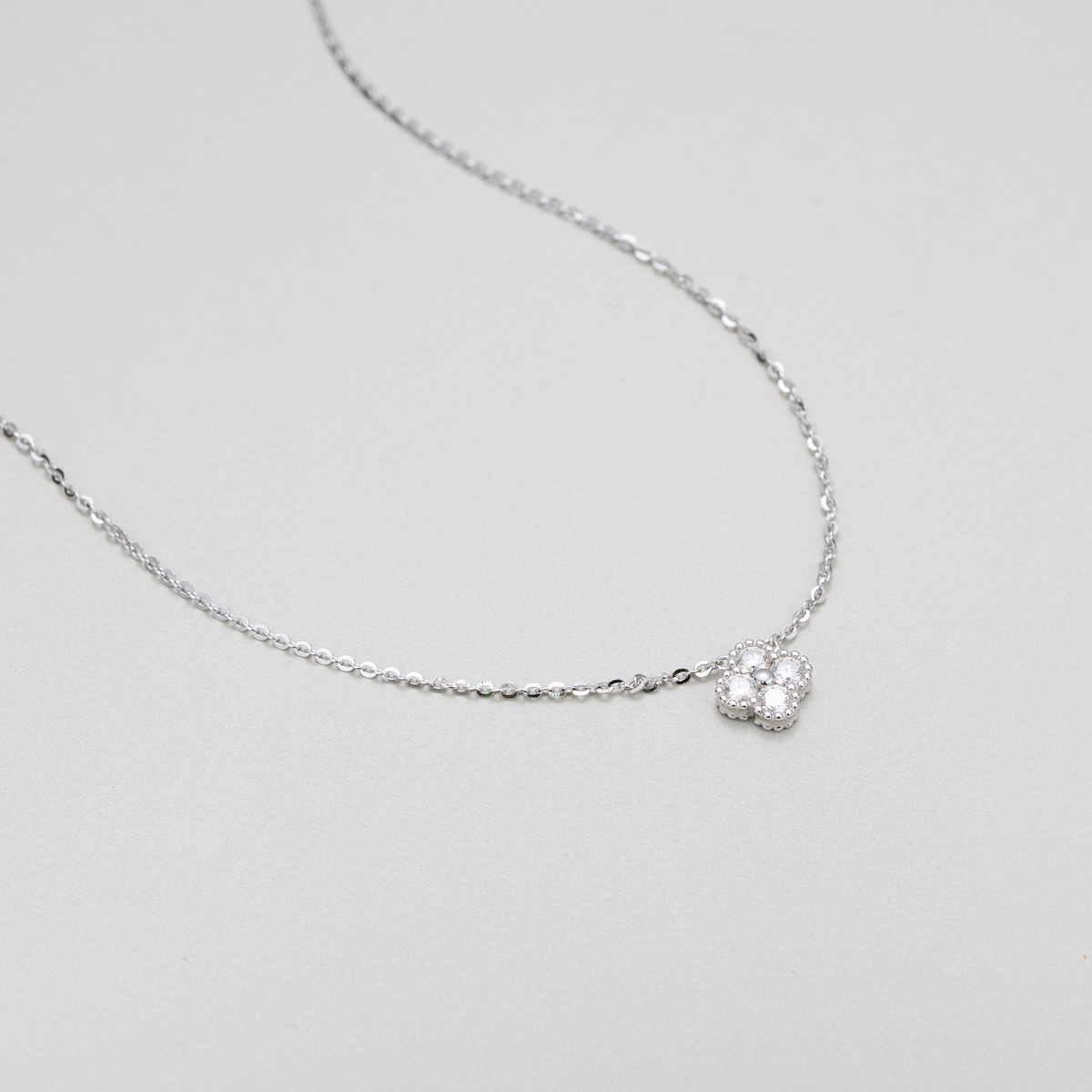 A delicate silver chain necklace featuring a small, textured silver heart-shaped pendant with a clear central gemstone, displayed on a neutral light gray background.