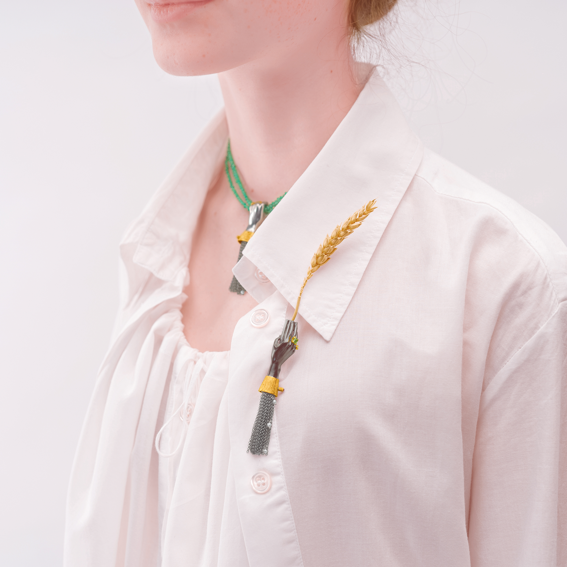 Model wearing black hand brooch with gold and gemstone details on white shirt, contemporary designer jewellery styling