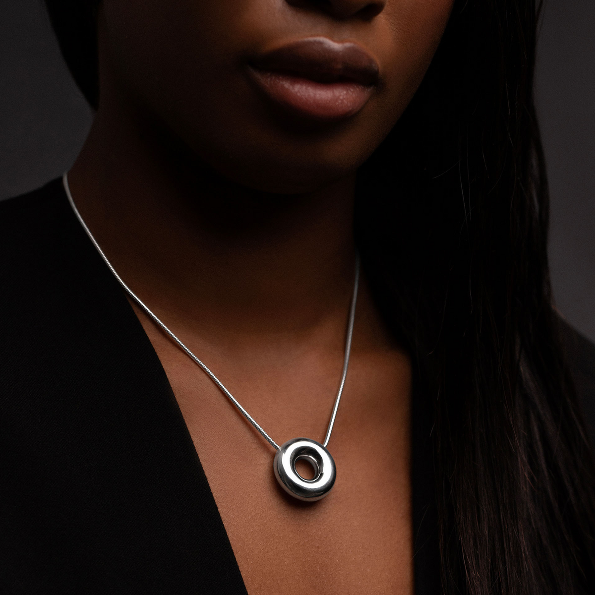 Model wearing the handcrafted Statement Monad Sterling Silver Necklace with a polished torus pendant and contemporary snake chain.