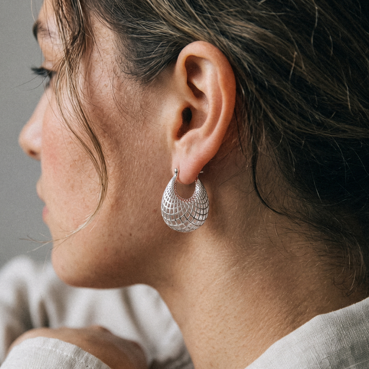 A close-up side profile of a woman wearing a textured silver crescent hoop earring.