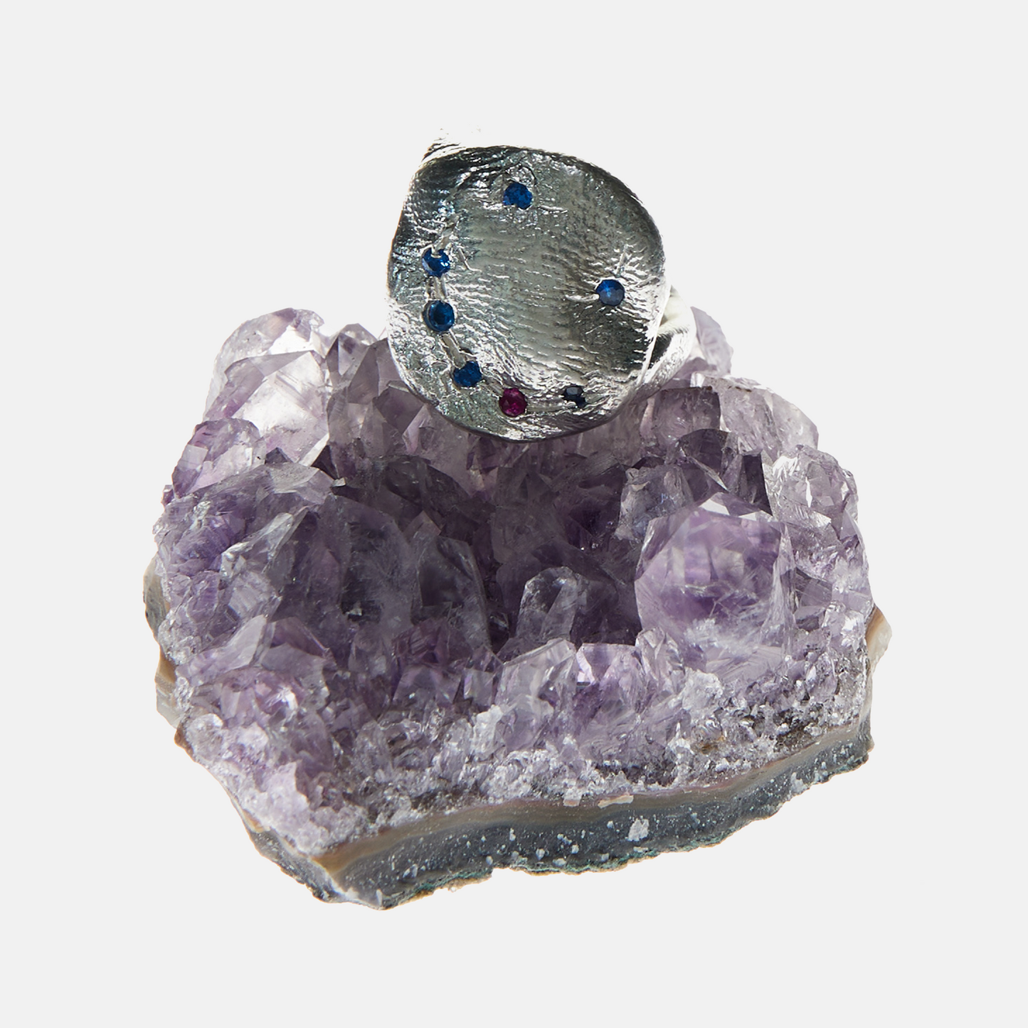 Silver ring with embedded gemstones on a purple crystal base
