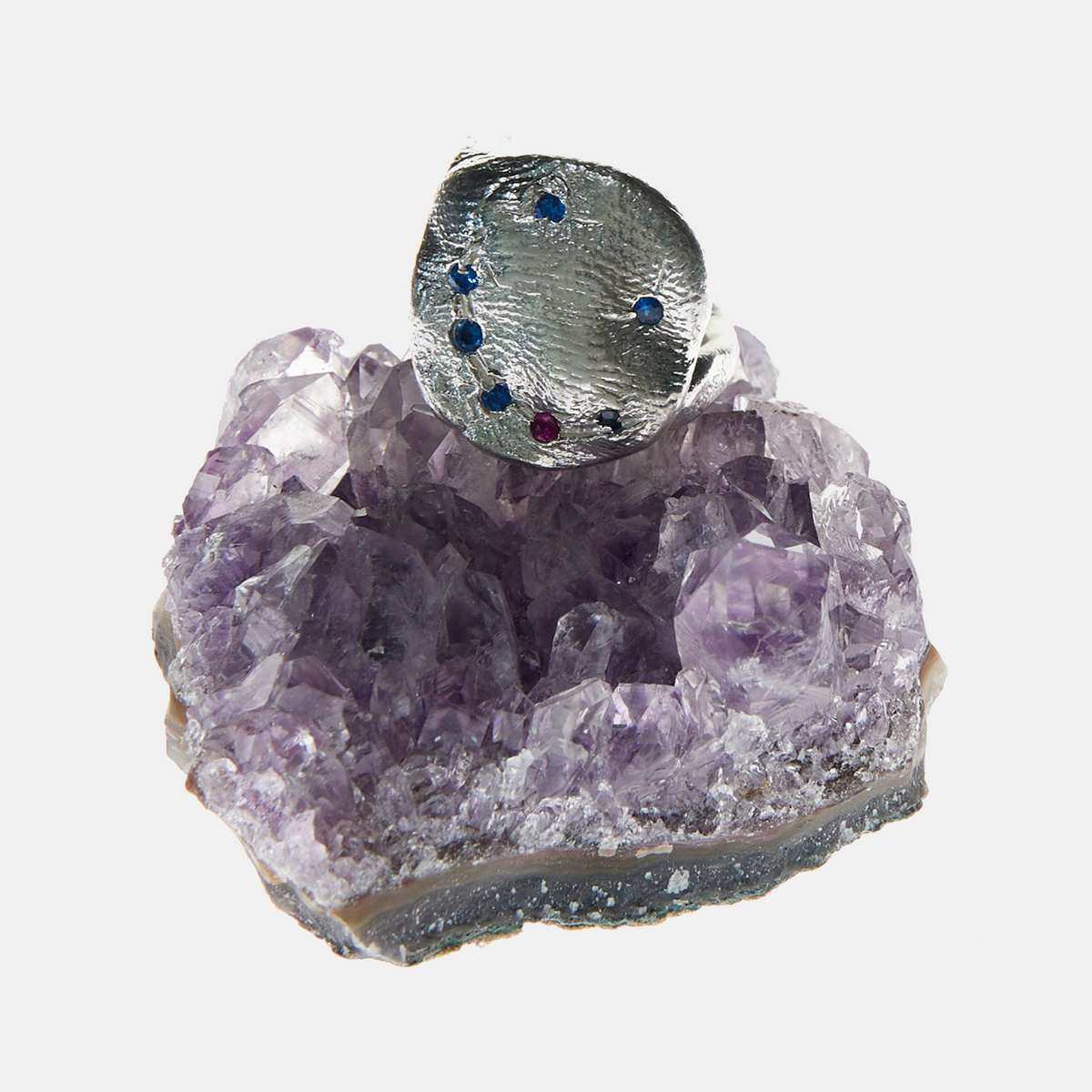 Silver ring with embedded gemstones on a purple crystal base