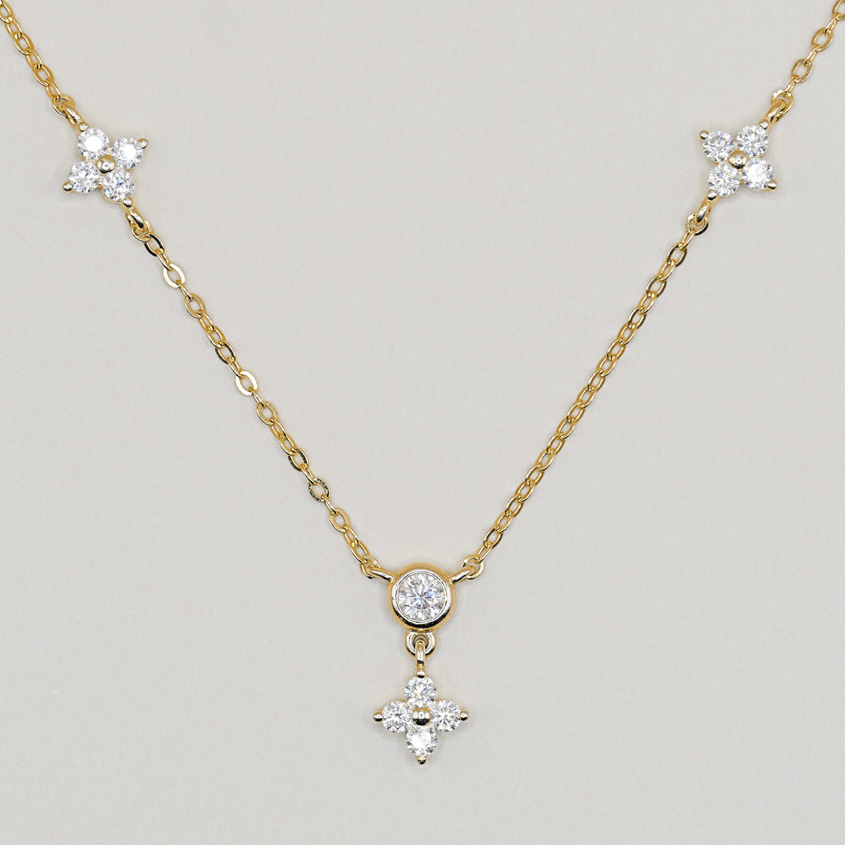 A delicate yellow gold chain necklace featuring three star-shaped clusters of clear stones, with a central round clear stone and a dangling four-pointed star pendant, shown on a neutral light gray background.