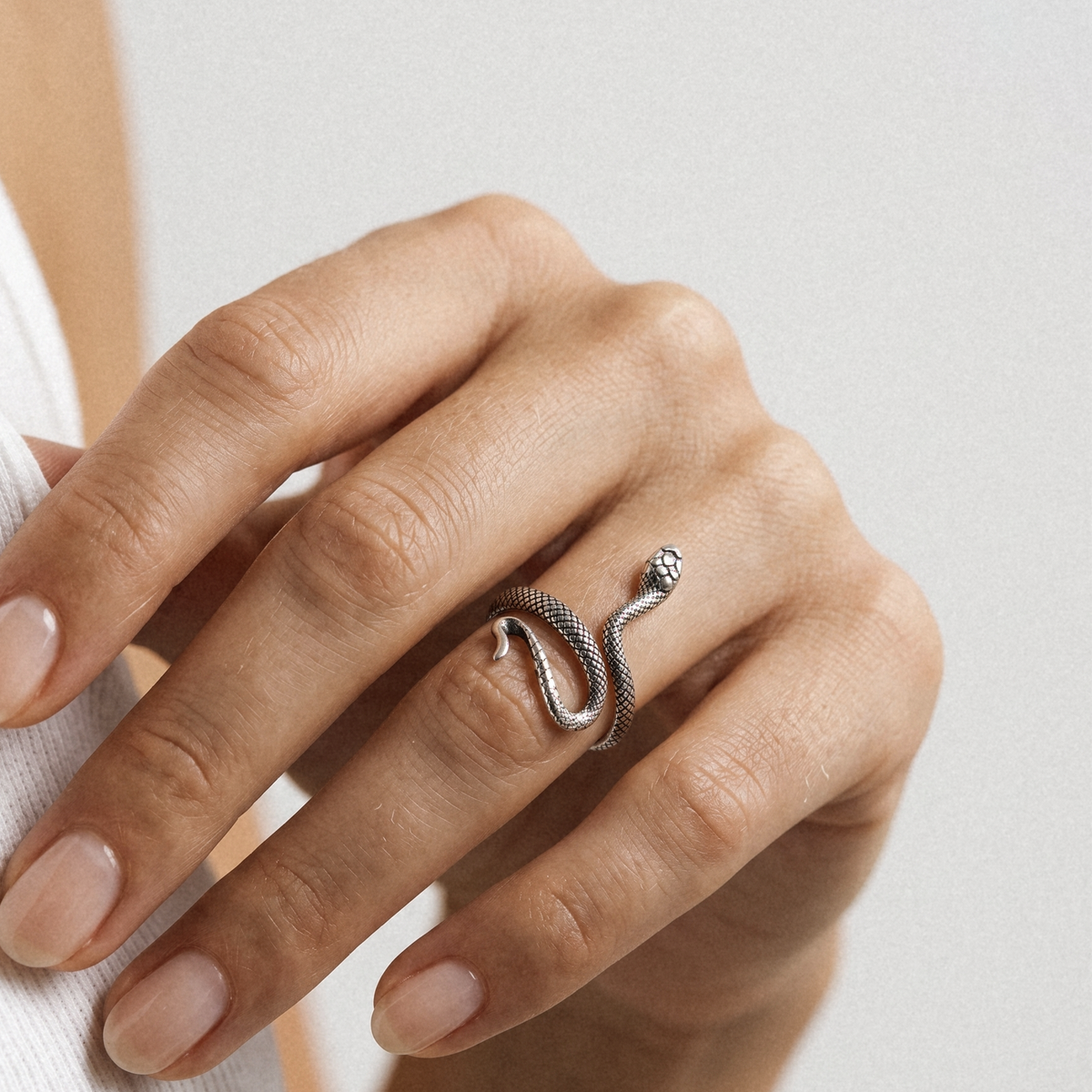 A close-up of a hand wearing a silver snake ring, with the fingers resting against a light neutral background.