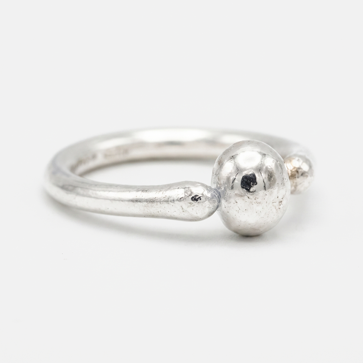 A sterling silver ring with a textured, organic-shaped band and a large, polished spherical bead on the front, set against a plain light gray background.