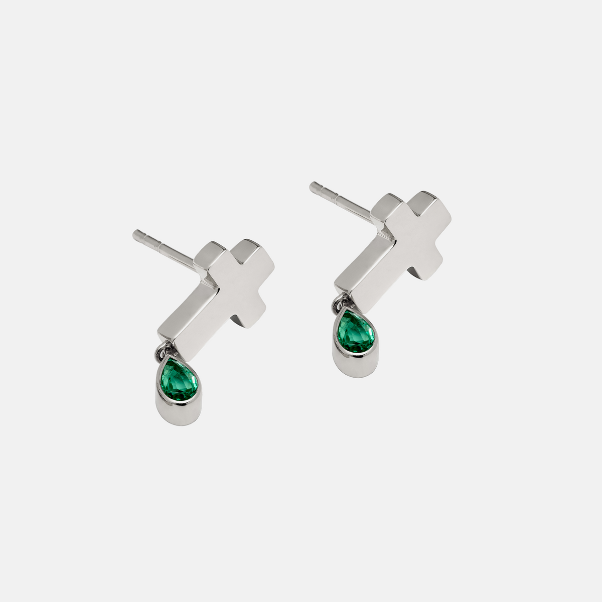 A pair of silver stud earrings featuring a small cross charm with a dangling teardrop-shaped green gemstone, shown on a light gray background.