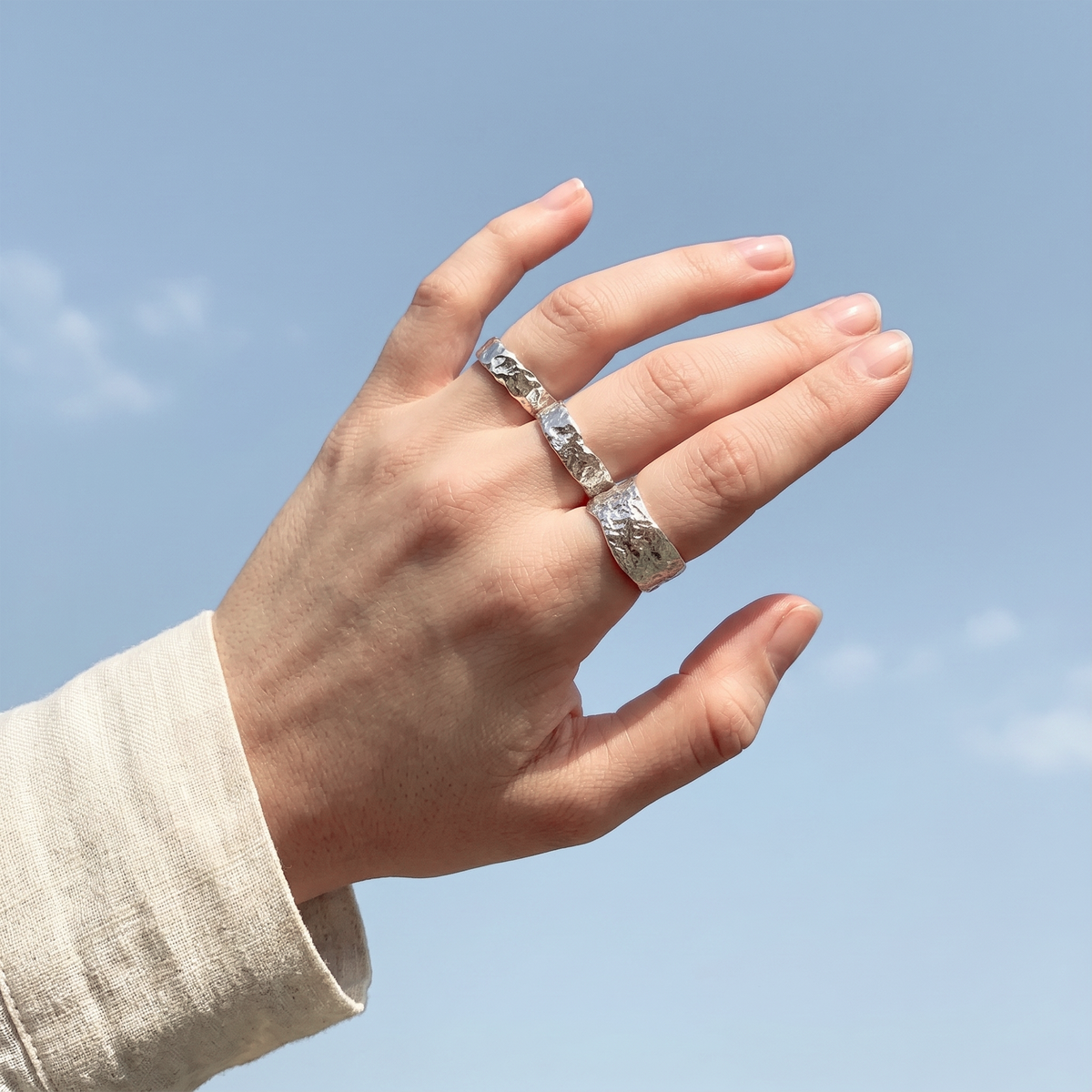 Hand wearing a silver ring against a clear blue sky