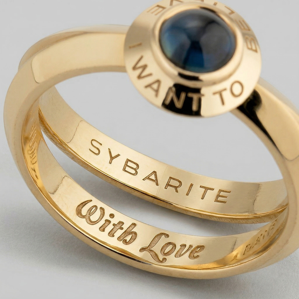 Close-up 18k gold rings with blue gemstone and engraved words, fine jewellery detail by Sybarite